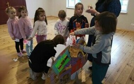 Dzieci przyklejają odbite dłonie na sylwetę jeża